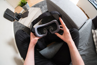 High angle view of man holding virtual reality siimulatoor while siting on sofa