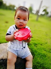 Portrait of baby boy with red toy on grassy field