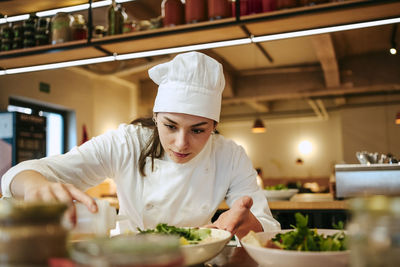 Close-up of female chef pouring dressing oil on salad at commercial kitchen