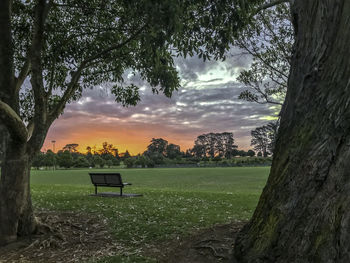 Empty bench on field against sky during sunset
