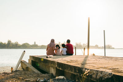 People sitting by lake against clear sky