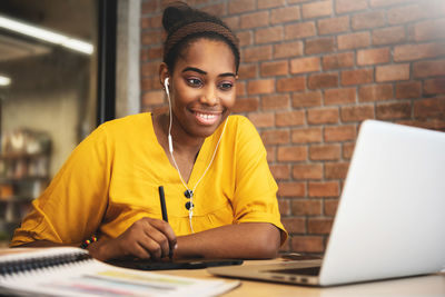 Portrait of smiling young woman using phone while sitting on table