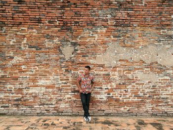 Young man standing against brick wall