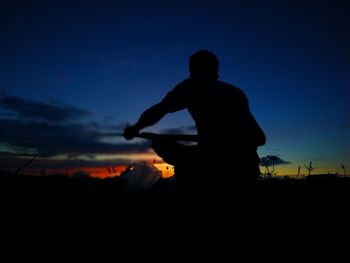 Silhouette man standing on field against sky at sunset