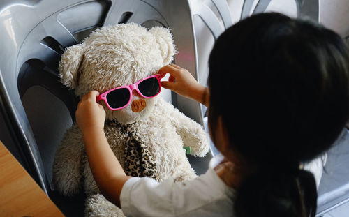 High angle view of girl wearing sunglasses to stuffed toy on chair
