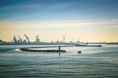 Scenic view of sea with harbour entrance against city skyline during sunset