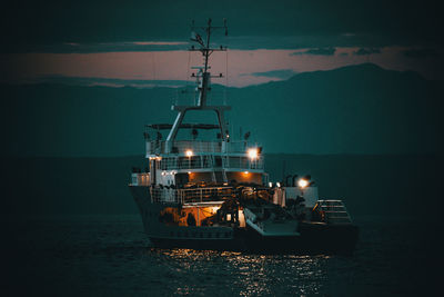 Illuminated ship in sea against sky at dusk
