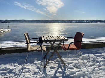 Empty chairs on snow covered land against sky