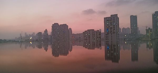 Reflection of buildings in lake against sky during sunset