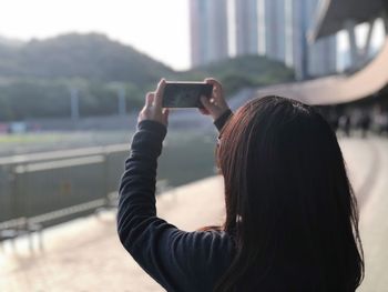 Rear view of woman photographing through smart phone against sky