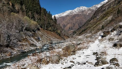 Scenic view of stream flowing through snow covered mountains