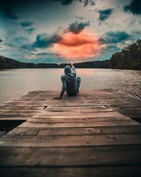 Man sitting on pier at beach against sky during sunset