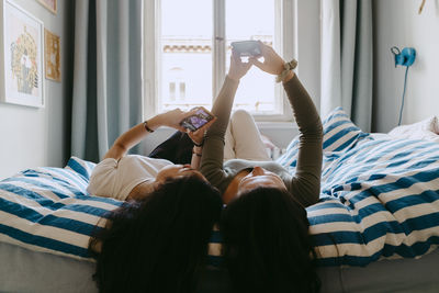 Female friends using smart phone while lying on bed at home