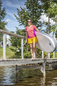 Full length of woman holding paddleboard on jetty over lake