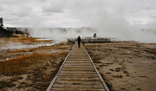 Rear view of man standing on footbridge amidst fog