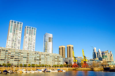 Buildings by river against clear blue sky at puerto madero