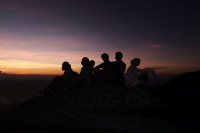 Silhouette people on landscape against sky at sunset