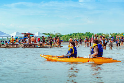 People with boats in sea against sky