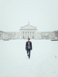 Full length of man standing on snow covered field against built structure