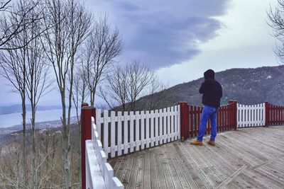 Rear view of man standing by railing against sky