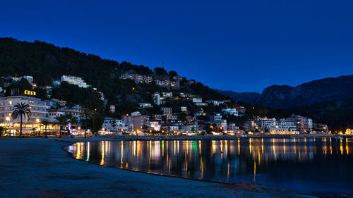 Illuminated buildings by river against sky at night