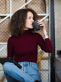 Portrait of young beautiful curly brunette woman drinking coffee while sitting at table in cafe.