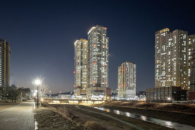 Illuminated buildings by street against sky at night