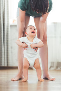 9-months old baby makes first attempts to walk. little child in white onesie with his mom. family.