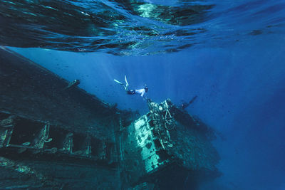 Man swimming underwater near abandoned ship in sea