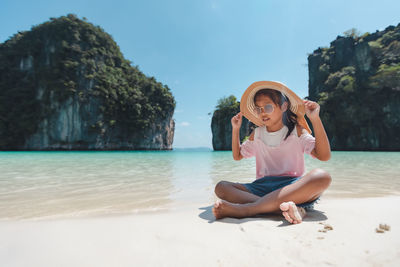 Full length of girl wearing hat sitting on beach
