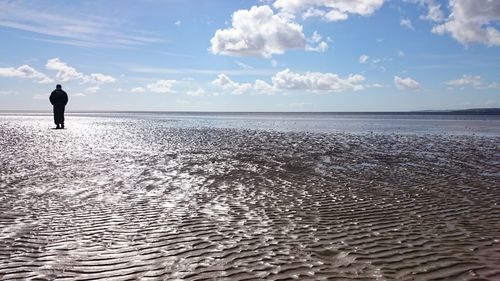 Rear view of silhouette man standing at sandy beach against sky