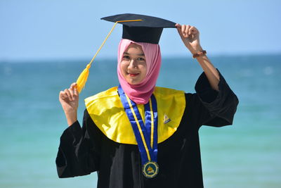 Portrait of woman in hijab wearing mortarboard while standing against sea