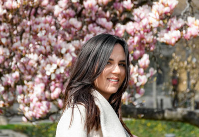 Portrait of beautiful young woman in front of pink magnolia tree.