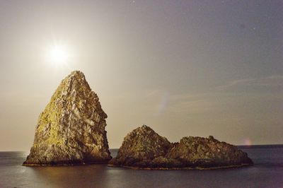 Rocks in sea against sky during sunset