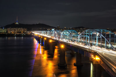 Illuminated bridge over river against sky in city at night
