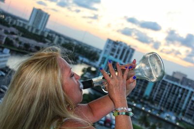 Side view of woman drinking through bottle in city during sunset