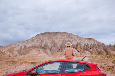 Rear view of woman sitting on mountain against sky