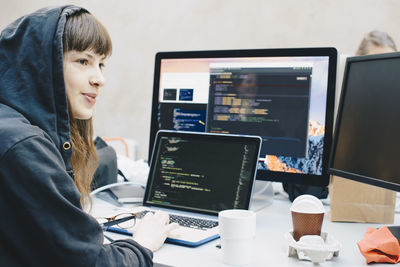 Side view of female computer programmer looking away while using laptop at desk in office