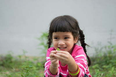 Smiling girl holding leaf while crouching against wall