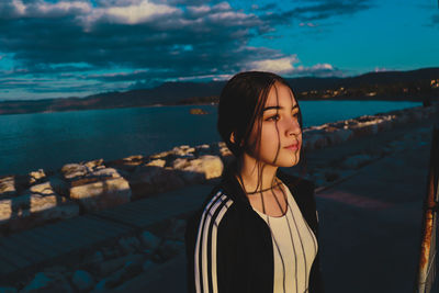 Girl looking away while standing against sea at dusk