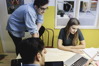 High angle view of three people using laptop at desk in board room