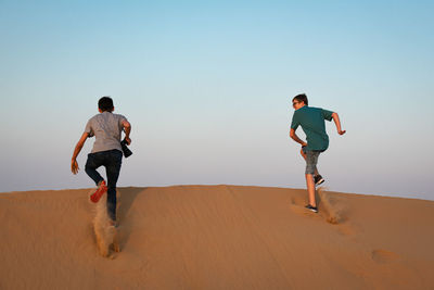 Full length of people running on sand dune against clear sky