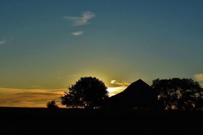 Silhouette trees and houses against sky during sunset