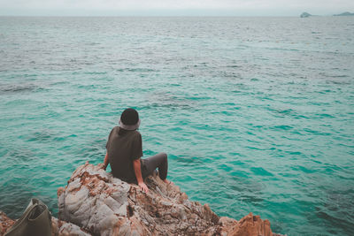 Rear view of man sitting on rock by sea