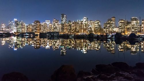 Illuminated buildings by sea against sky at night