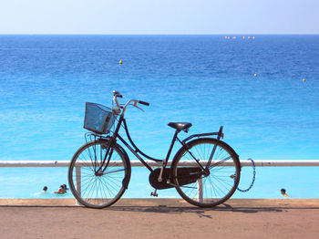 Bicycle by sea against clear blue sky
