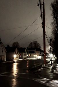 Illuminated street by buildings against sky at dusk