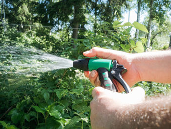 Hairy man's hands holding nozzle of watering hose