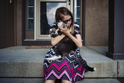 A pre teen girl snuggling her cat on the front porch of her house