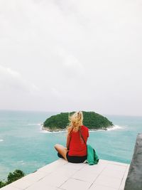 Rear view of woman sitting by sea against sky